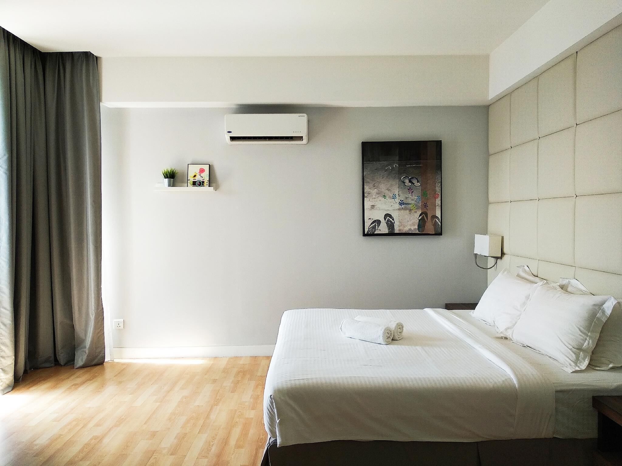 Ein Hotelzimmer mit Bett, Wandklimaanlage, einer kleinen Ablage mit Dekoration und einem Gemälde.