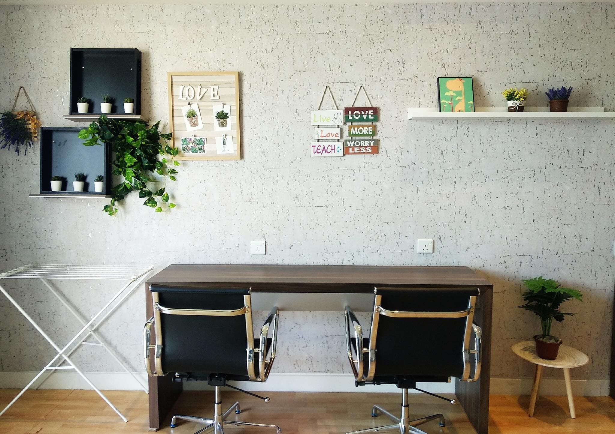 A modern office space with a wooden desk, two black office chairs, and a small round table with a potted plant.