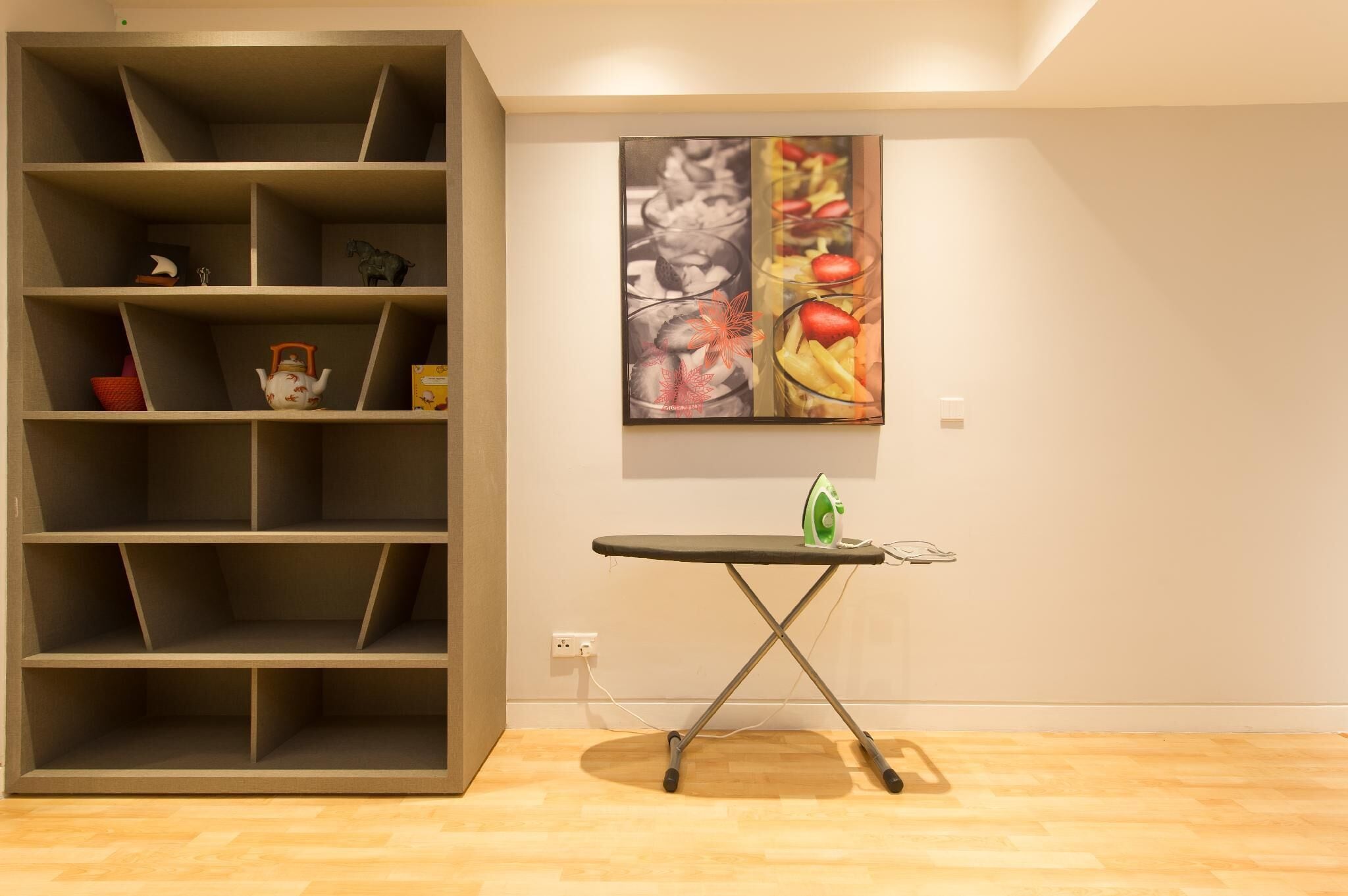 A room with a large open shelving unit, a small ironing board, and a wall-mounted painting.