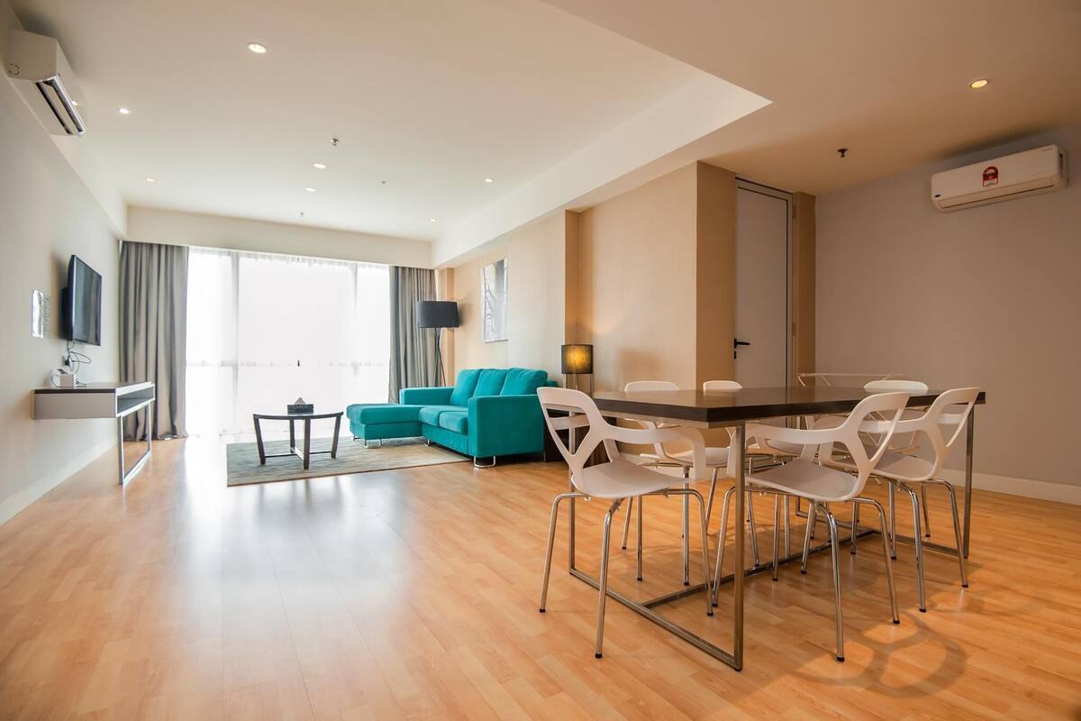 A modern living room with a teal sofa, a dining table with white chairs, and a flat-screen TV mounted on the wall.