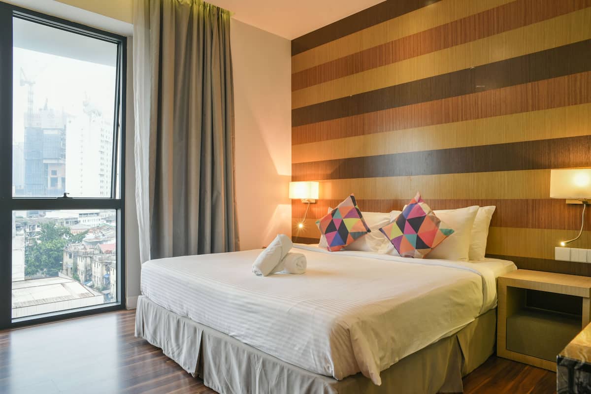 A hotel room with a large window, a bed with white bedding, striped wallpaper, and two bedside lamps.