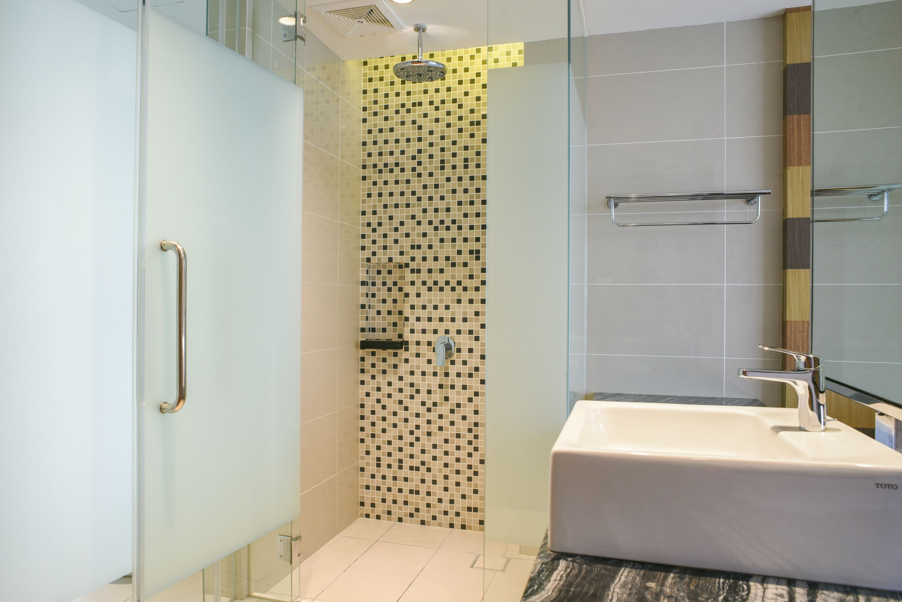 Un baño moderno con cabina de ducha de vidrio, un lavamanos blanco y una pared de azulejos con diseño a cuadros.