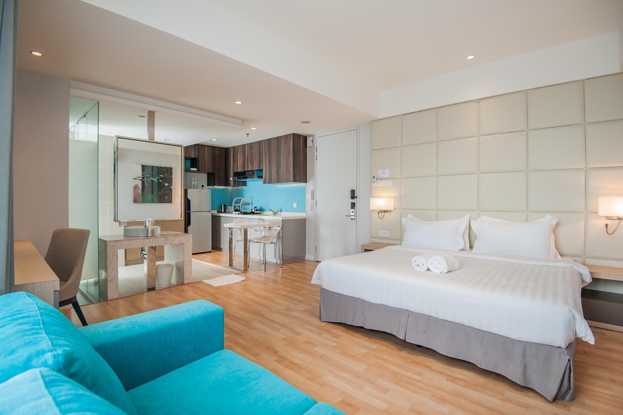 A modern hotel room with a large bed, a desk, a kitchenette, and a bathroom.