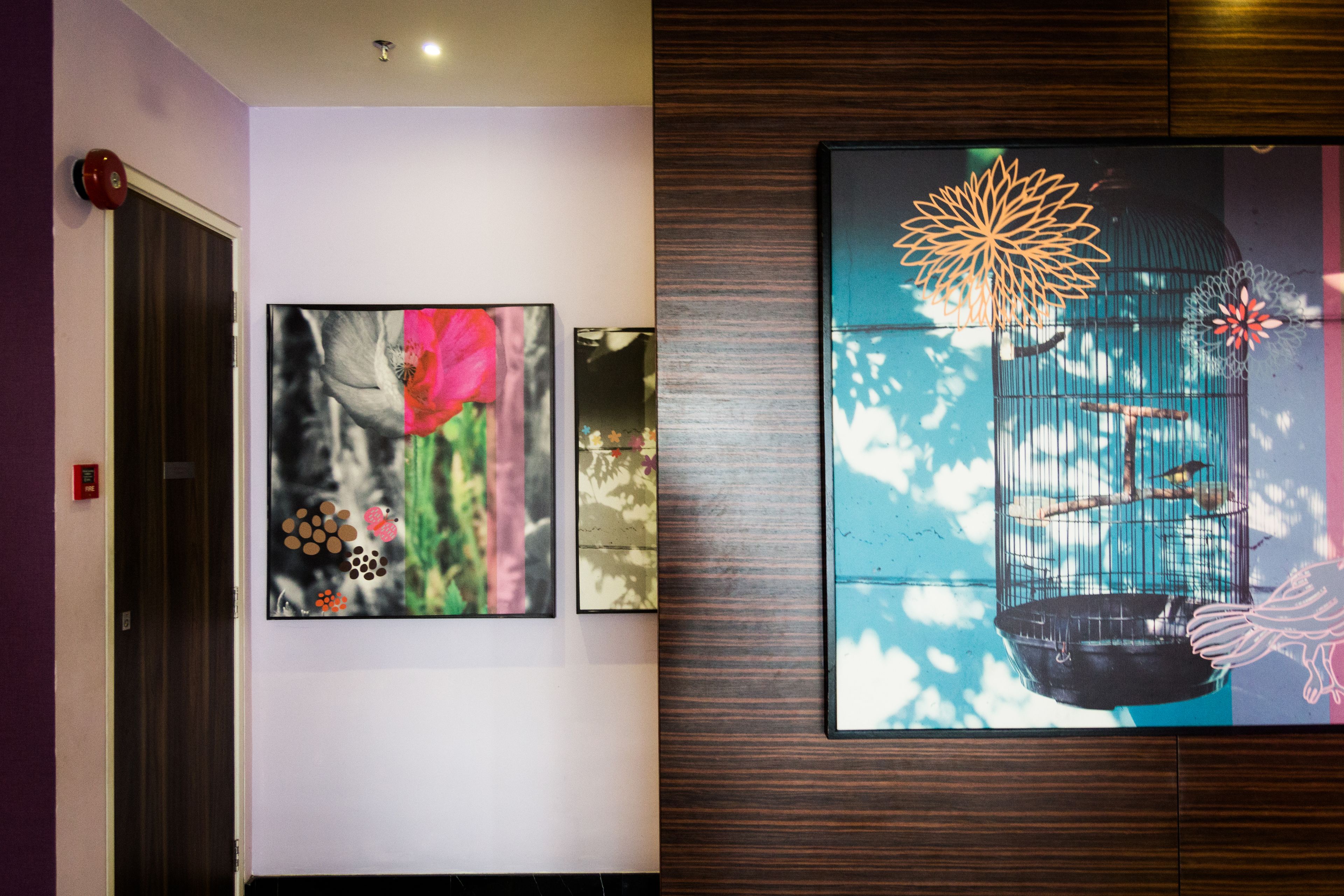A hallway with three framed artworks on the wall, a wooden panel, and a door with a red handle.