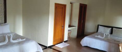 A hotel room with two beds, a wooden door, a small stool, and a mirror on the wall.