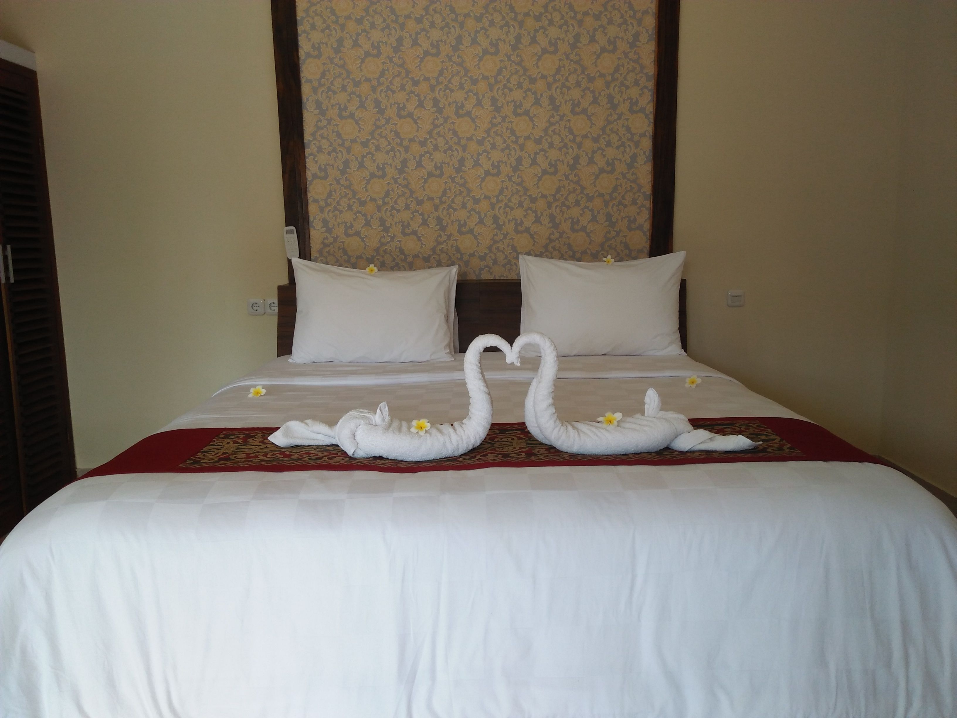 A hotel room with a neatly made bed, two pillows, and a floral-patterned wall.