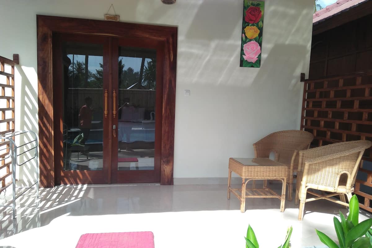 A room with a sliding glass door, wicker furniture, a pink mat, and a wall-mounted flower decoration.