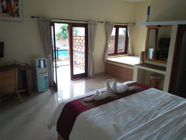A hotel room with a bed, a desk, a chair, a water dispenser, and a window with curtains. - Villa Kinagu (Gili Meno)
