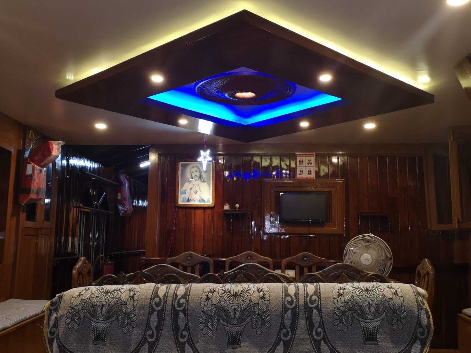 A room with a wooden ceiling, a TV mounted on the wall, and a fan on the floor.