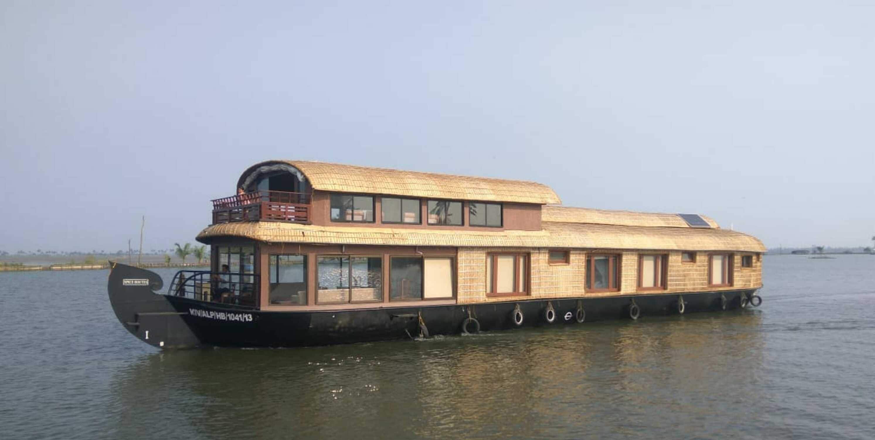 A houseboat with a thatched roof, multiple windows, and a small deck area.