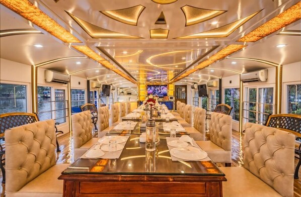Uma área de refeições luxuosa, com uma mesa comprida posta para uma refeição, rodeada por assentos confortáveis.