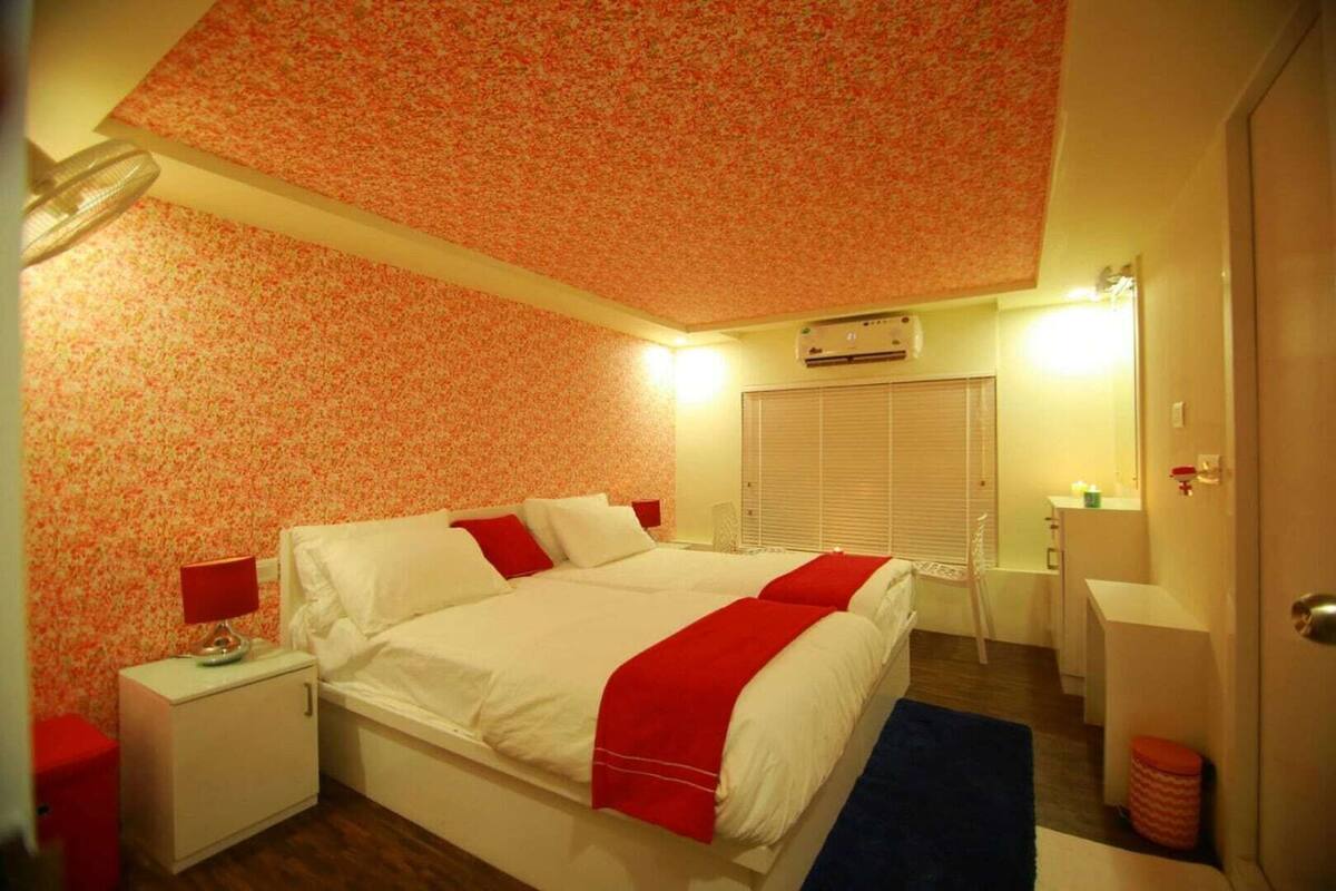 Un dormitorio con cama, mesitas de noche, un espejo, una ventana con persianas y una zona de baño pequeña.