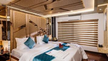 A hotel room with a large bed, a headboard with a geometric pattern, a bedside table with a lamp, and a window with blinds.