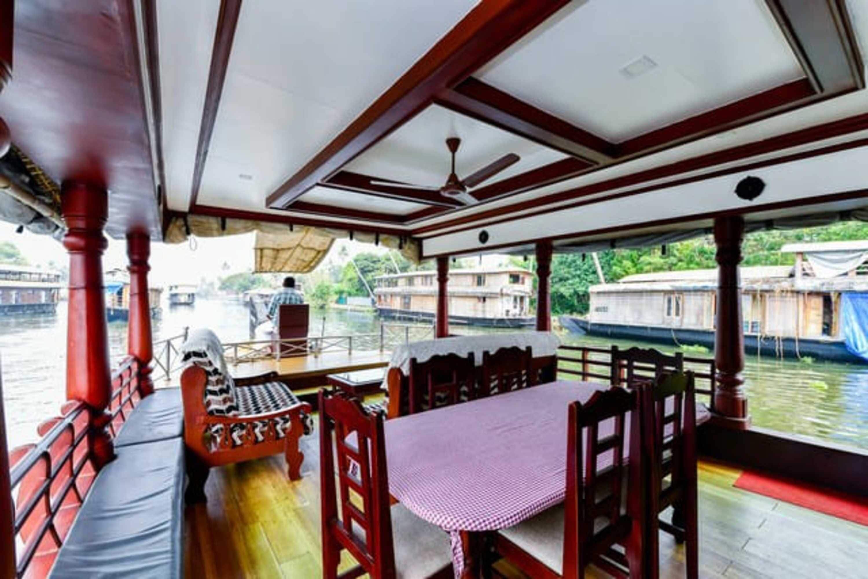 Comedor en un barco con una mesa, sillas, un banco y vista al río.