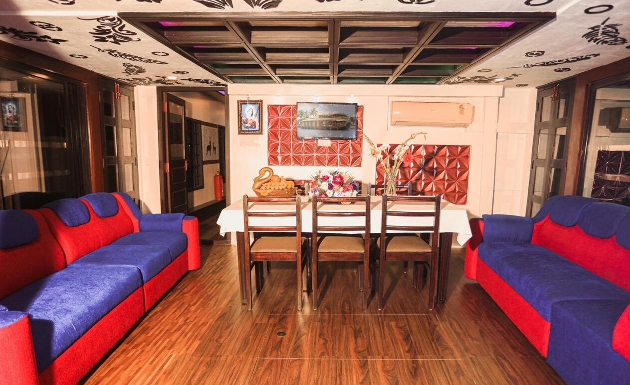 A room with a wooden floor, a dining table with chairs, and two sofas with red and blue cushions.