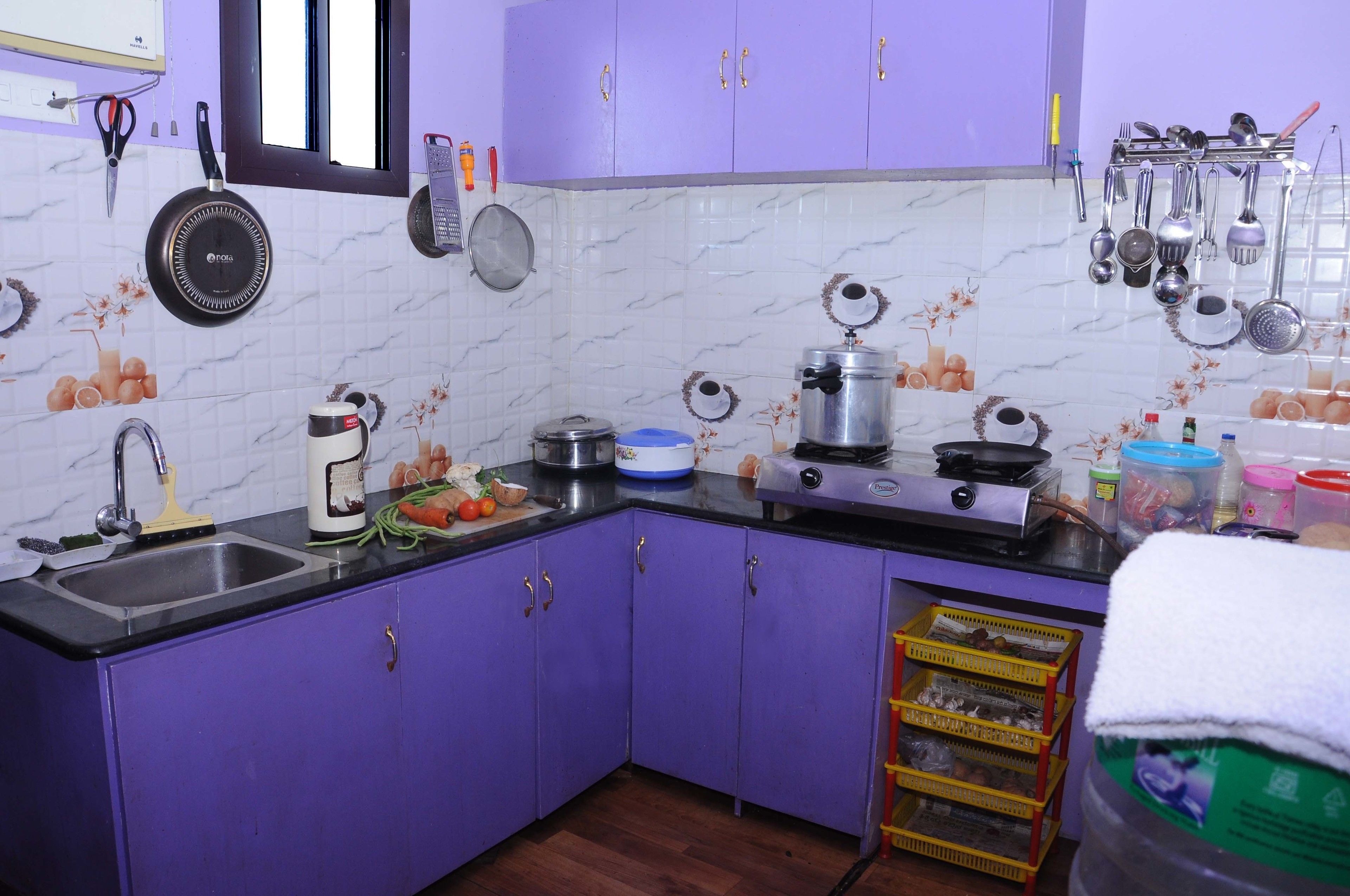 Una cocina con gabinetes morados, un fregadero, una estufa y diversos utensilios y electrodomésticos.
