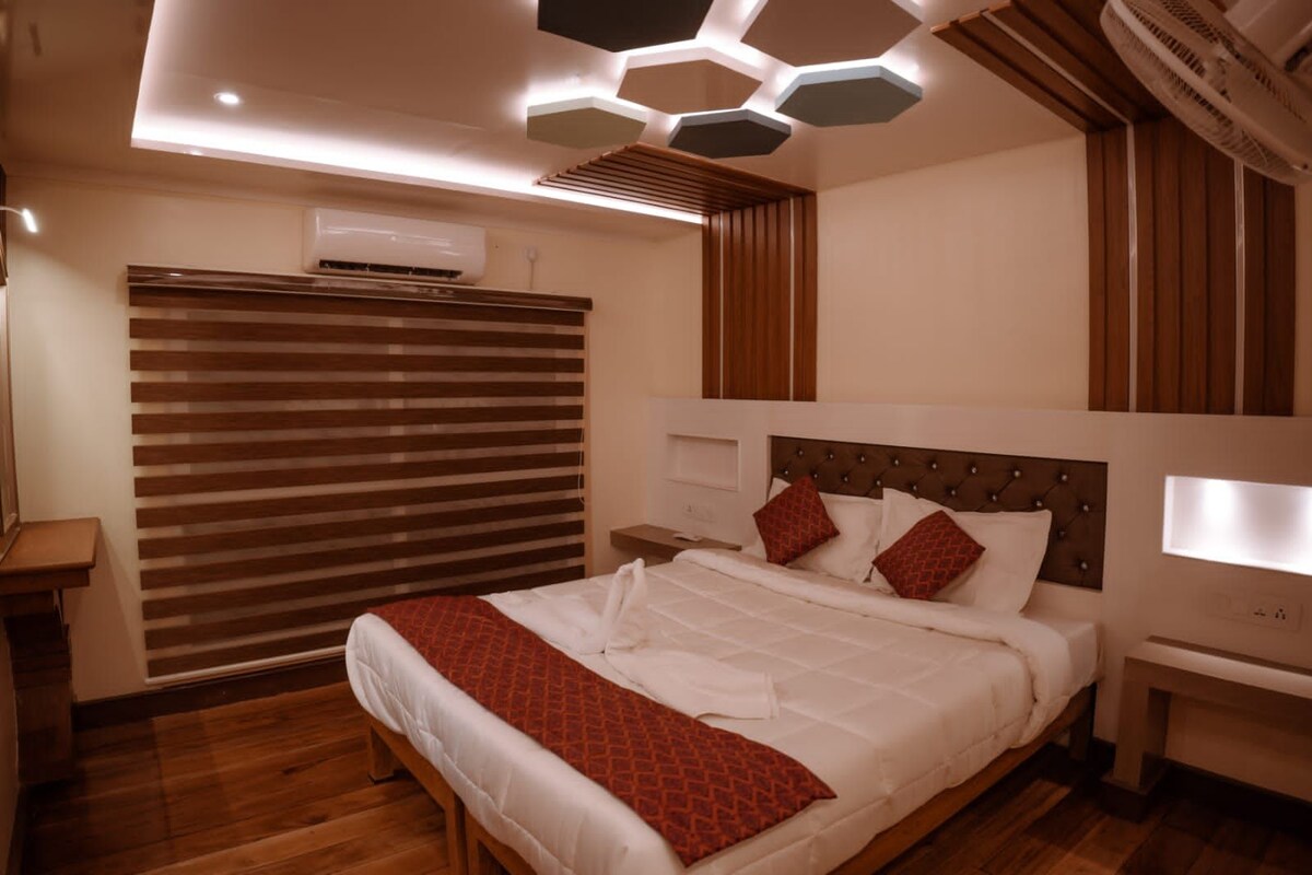 A modern bedroom with a large bed, wooden flooring, a slatted window blind, and a unique hexagonal ceiling design.