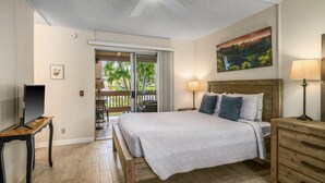 Une chambre à coucher avec un lit, un téléviseur posé sur un meuble, un ventilateur de plafond, un tableau et un balcon aménagé avec du mobilier d’extérieur.