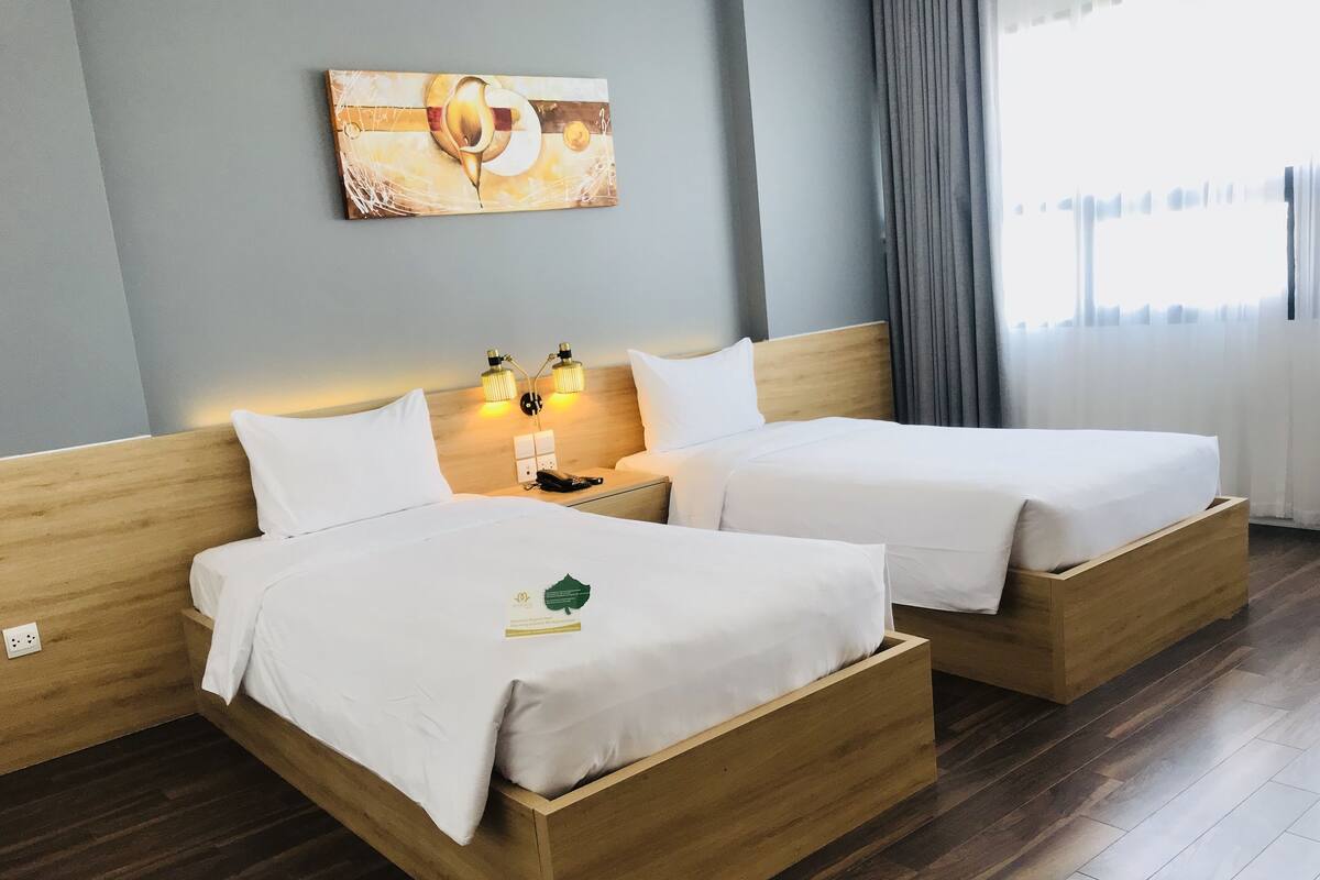 A hotel room with two wooden beds, a painting on the wall, and a nightstand with lamps.