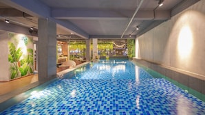 An indoor swimming pool with a tiled floor, surrounded by walls with greenery and seating areas. - Magnolia Hotel (Da Nang)