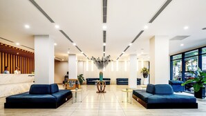 Een moderne lobby met een receptiebalie, twee banken, een decoratieve vaas en een groot raam.