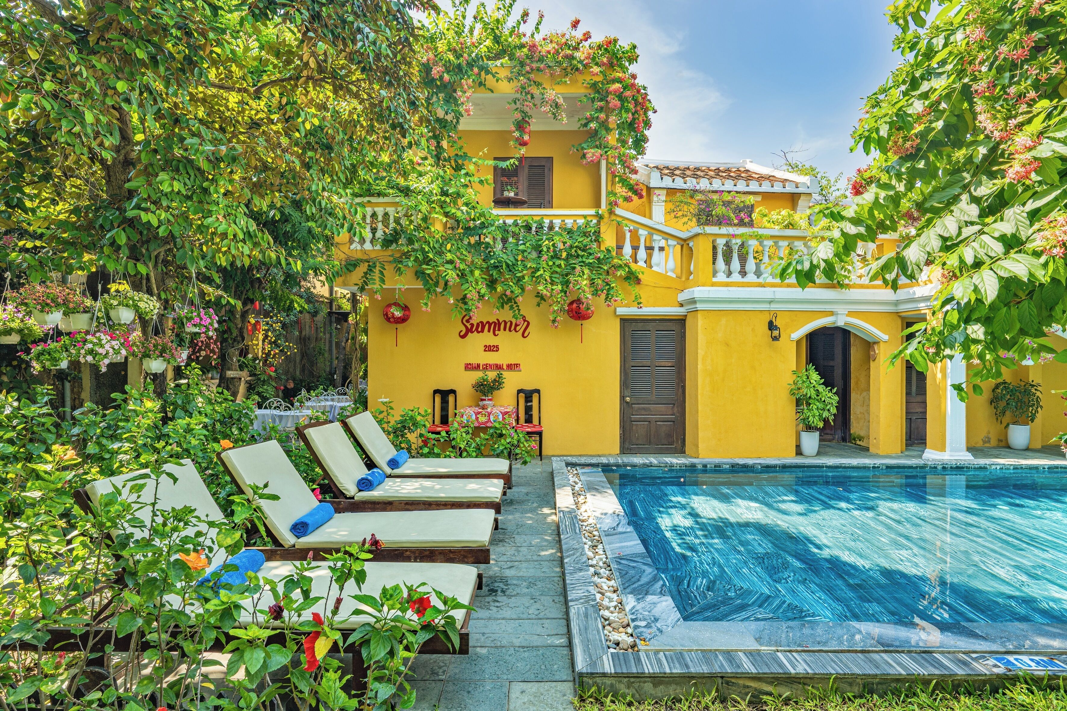 A yellow building with a pool, lounge chairs, and potted plants.