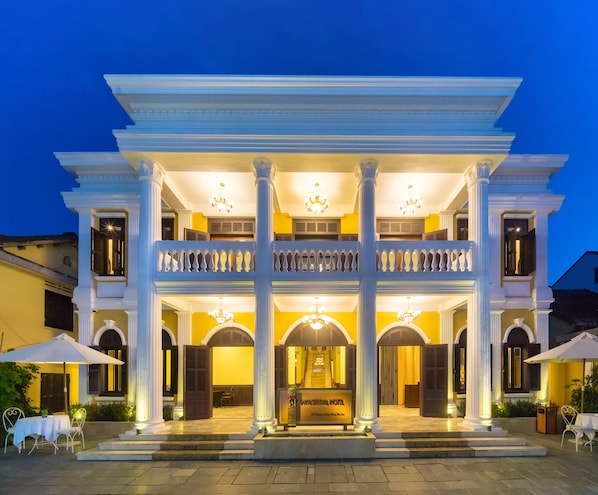 A grand hotel with a two-story facade, large columns, and a balcony with ornate railings.