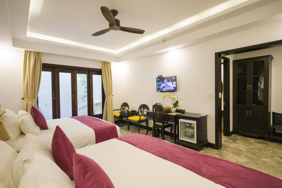 A hotel room with two beds, a desk with a computer, a television, and a door leading to another room.