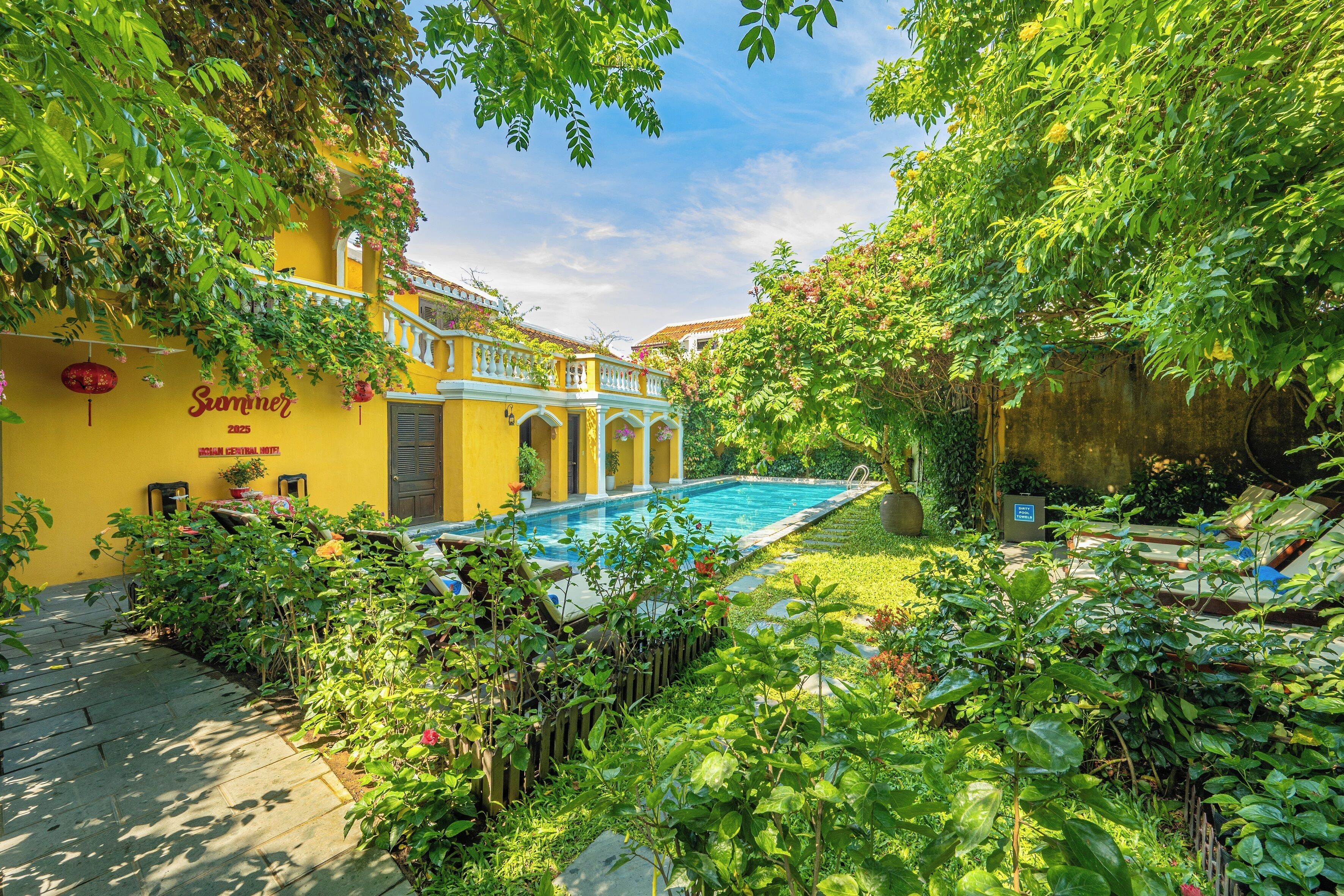 A yellow building with a swimming pool surrounded by lush greenery.