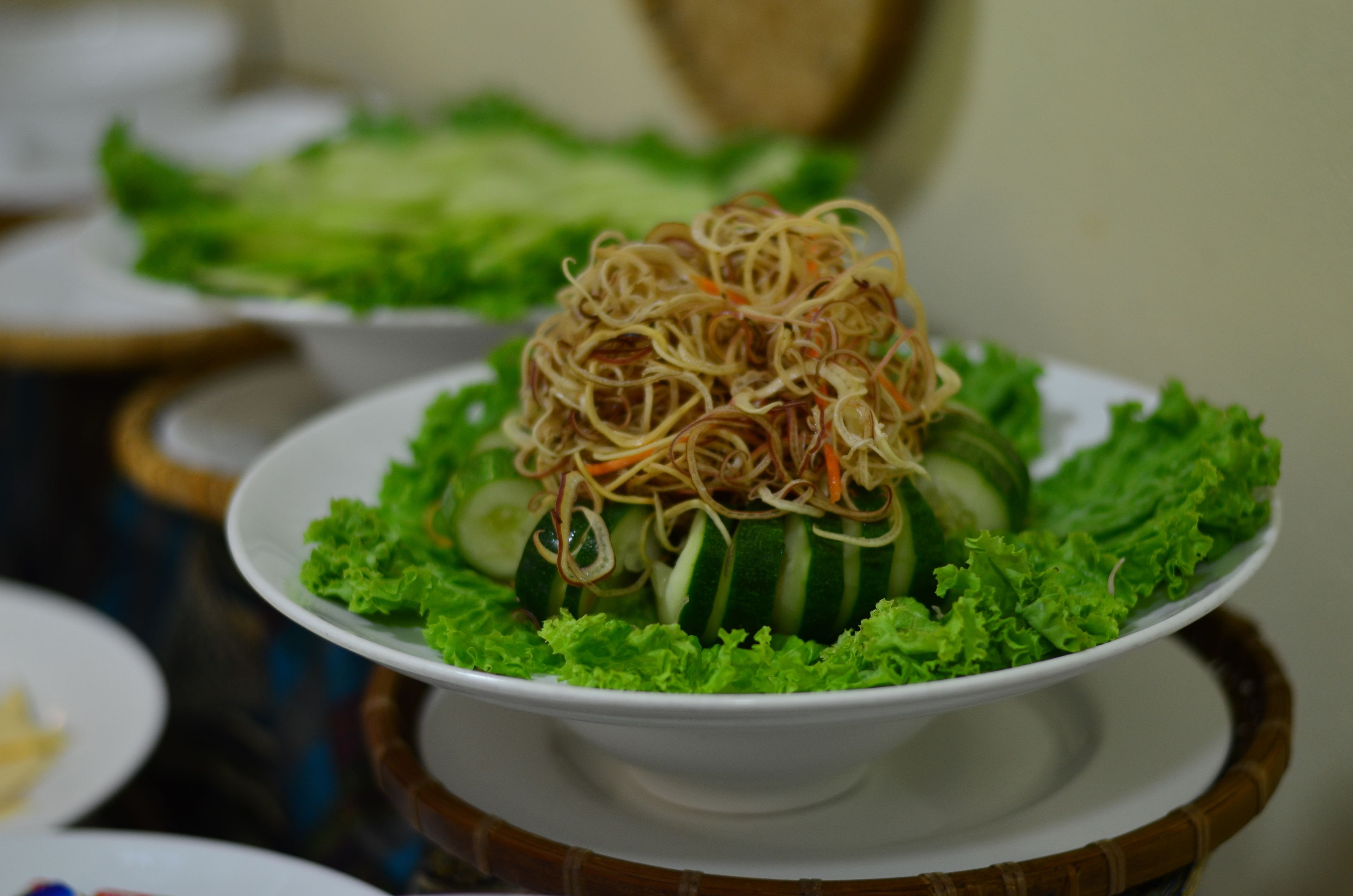 A bowl of noodles on a plate with lettuce and cucumber slices.