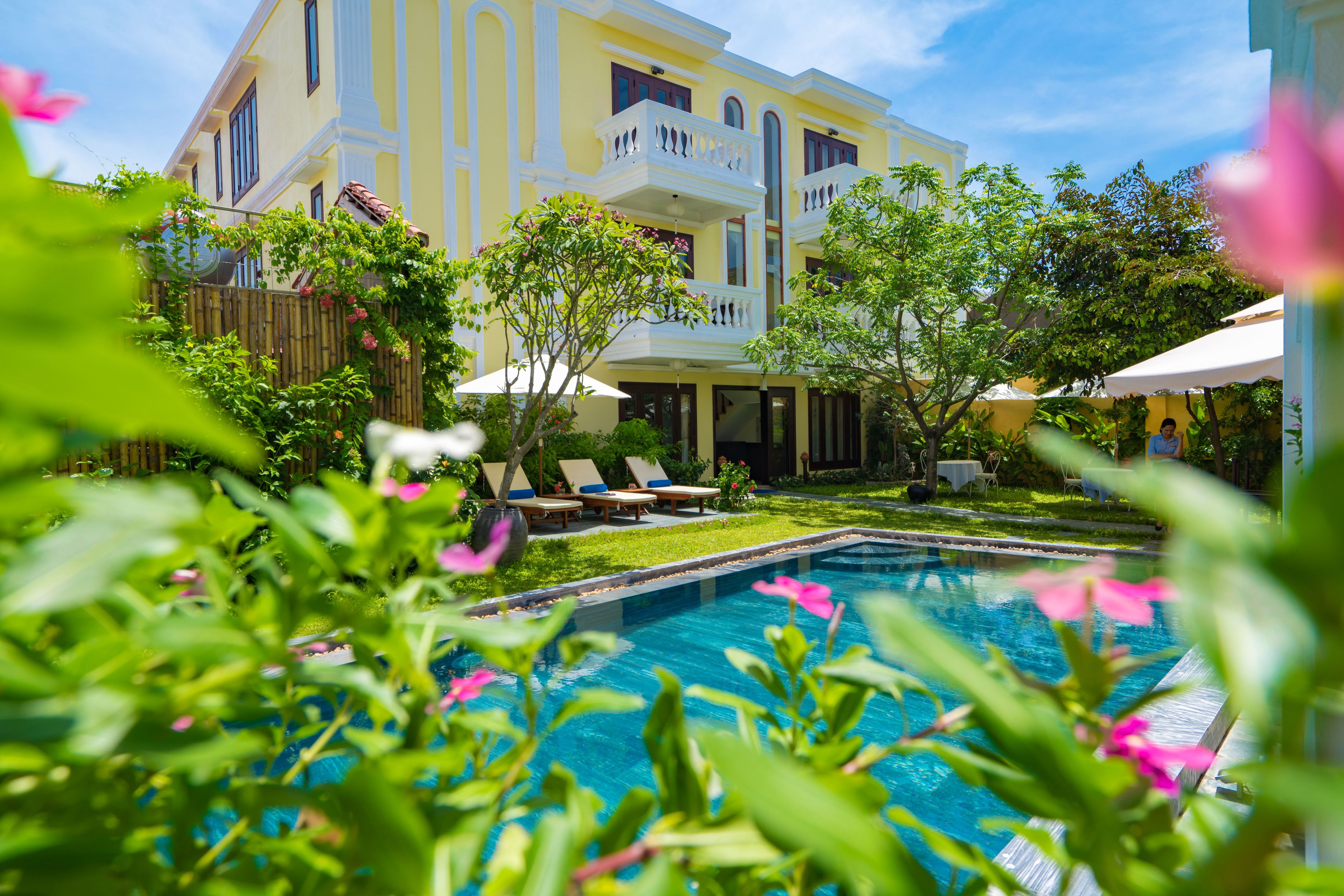 A large, yellow building with a swimming pool, surrounded by greenery and outdoor seating.