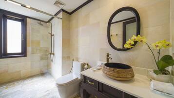 A bathroom with a glass-enclosed shower, a toilet, a sink with a large bowl, a mirror, and a potted orchid.