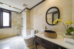 A bathroom with a glass-enclosed shower, a toilet, a sink with a large bowl, a mirror, and a potted orchid.