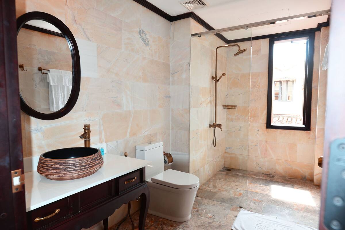 A bathroom with a marble wall, a round sink, a toilet, and a shower.