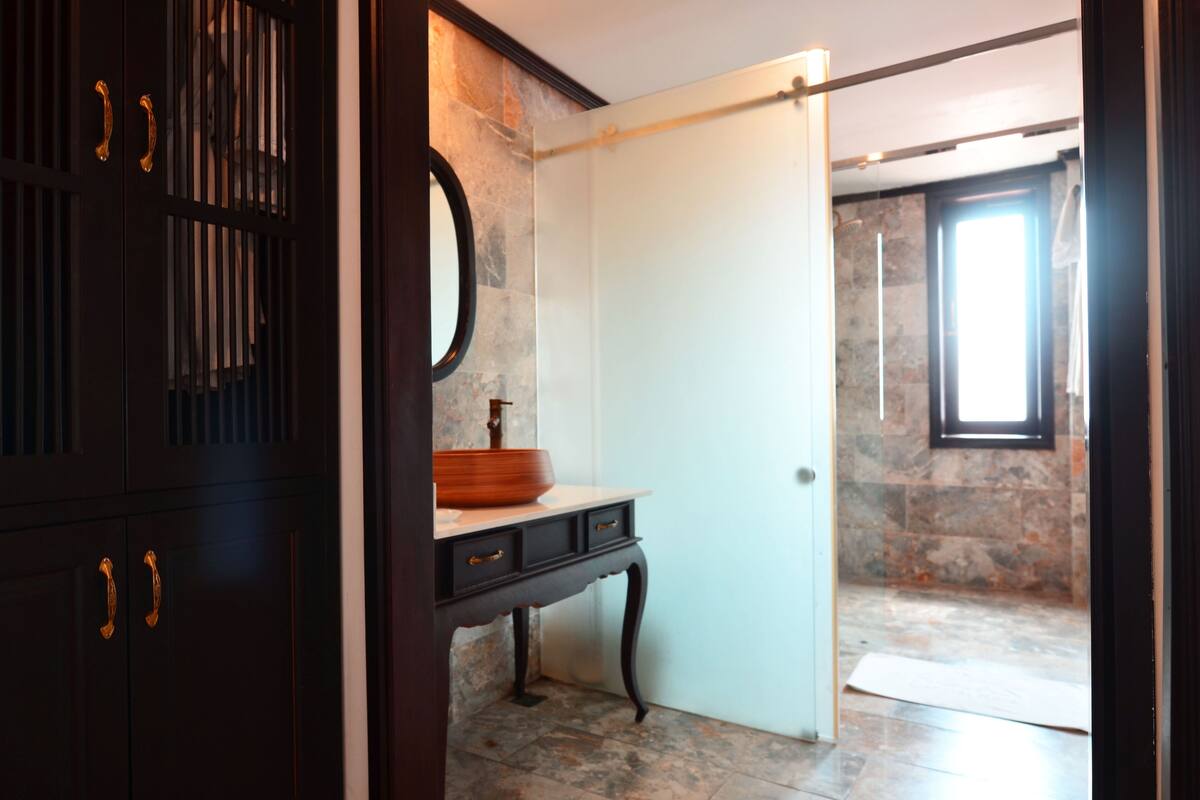 A bathroom with a dark wooden vanity, a round mirror, and a stone wall.