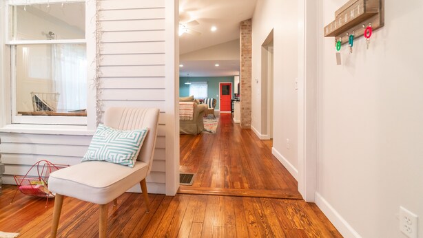 A room with a wooden floor, a white chair with a patterned cushion, and a window with a white curtain. - Walking Distance to Shops, Beach, Restaurants and Brewery  (New Buffalo)
