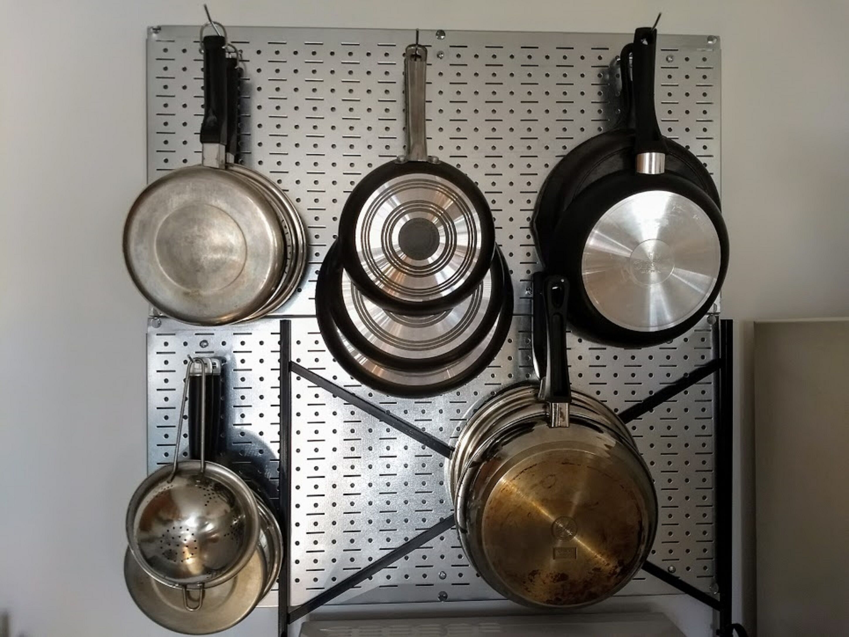 Una cocina con ollas y sartenes colgadas en una pared con panel perforado.