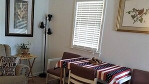 Un salon comprenant un canapé, deux fauteuils, une table basse, un lampadaire, un tableau encadré et une fenêtre avec des stores.