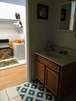 A small bathroom with a sink, mirror, and wooden cabinets. There is a chair and a small table with a towel and a basket. - Very clean & private (Bowling Green)