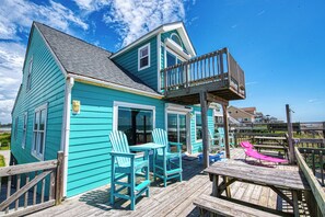 A turquoise two-story house with a deck, outdoor seating, and a wooden staircase.