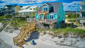 A beachfront house with a wooden staircase leading to a deck, surrounded by sand and vegetation. - Larry’s Lazy Susan: Steps to the Surf, Perfect for Paws & Sunsets Reduced Rates (North Topsail Beach)