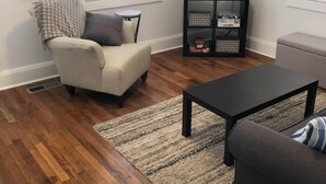 A living room with a beige armchair, a dark sofa, a coffee table, a TV, and a bookshelf. - 1 Block to the Beach, Fully Fenced in Backyard, Golf Cart Included (Myrtle Beach)