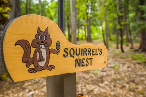 Een houten bord met een cartoon-eekhoorn en de tekst 'Squirrel's Nest'.