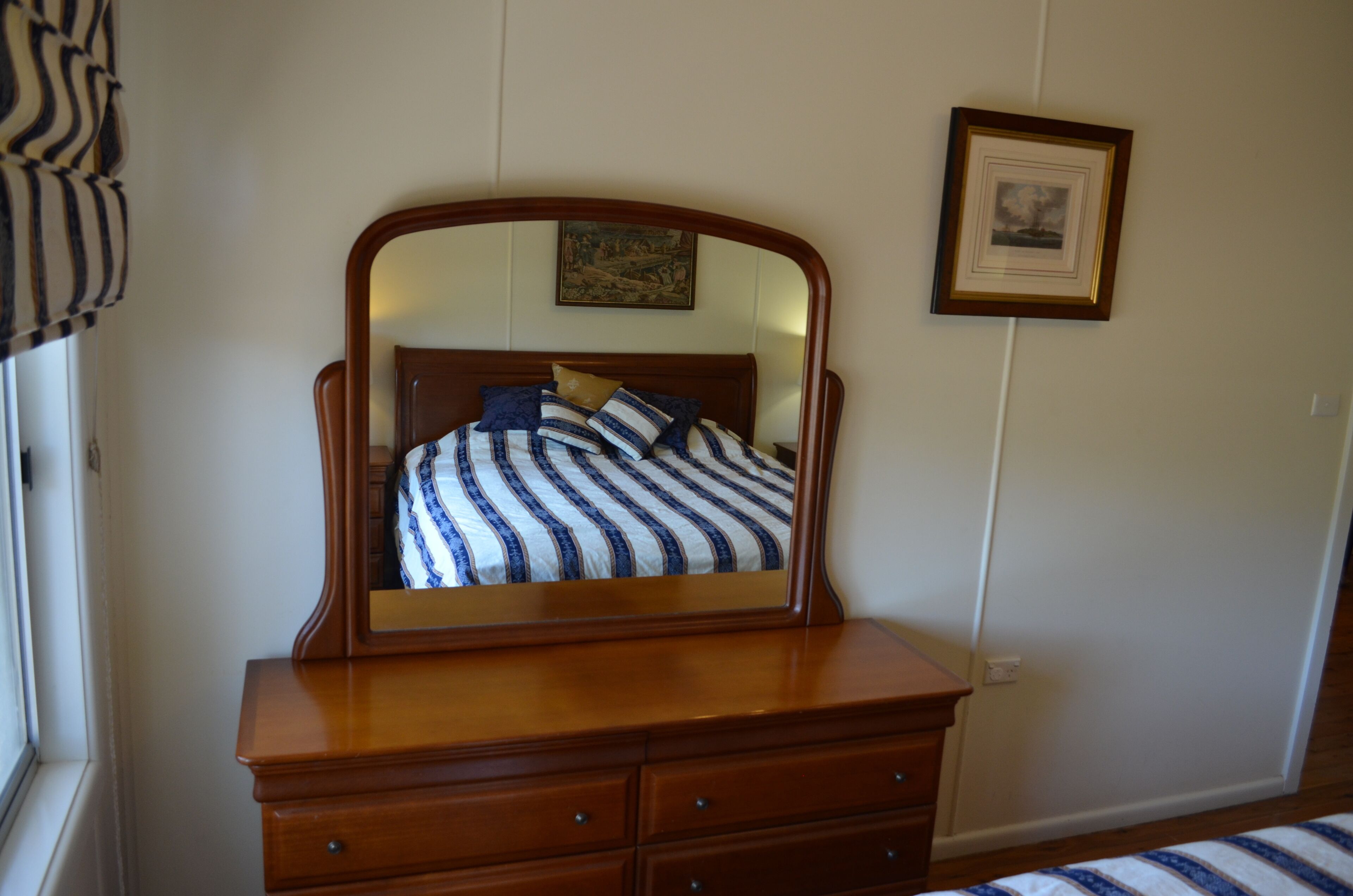 Un dormitorio con un aparador de madera, una cama con ropa de cama a rayas, un espejo y un cuadro en la pared.