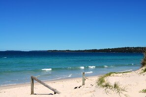 A beach with clear blue water, sandy shore, and a wooden fence.