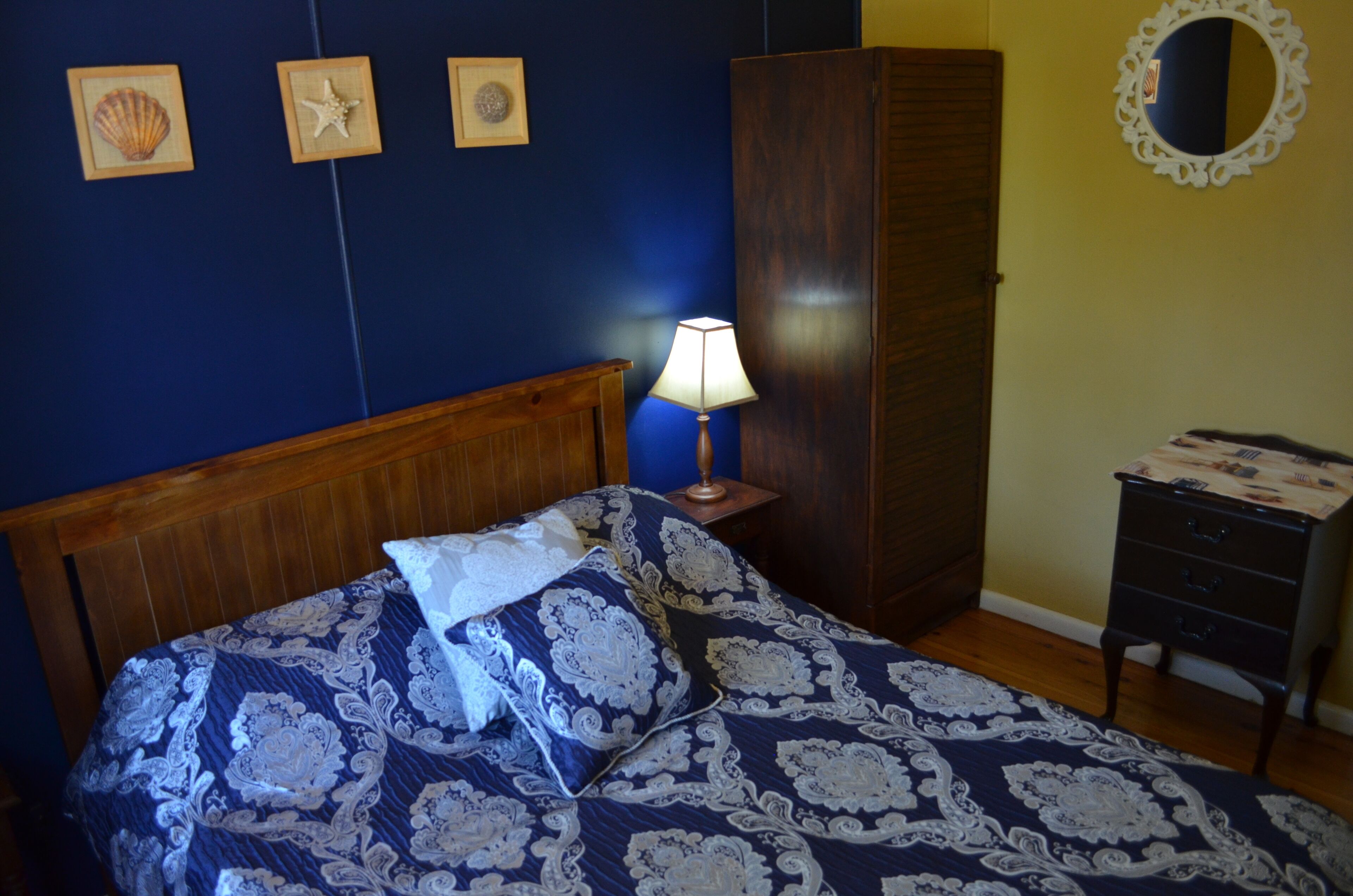 Un dormitorio con cama, mesita de noche, cómoda y adornos en la pared, incluyendo conchas enmarcadas y una estrella de mar.