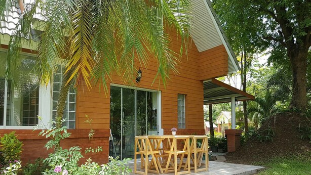Een modern huis met een houten gevel, een glazen voordeur en een terras met tuinmeubels.