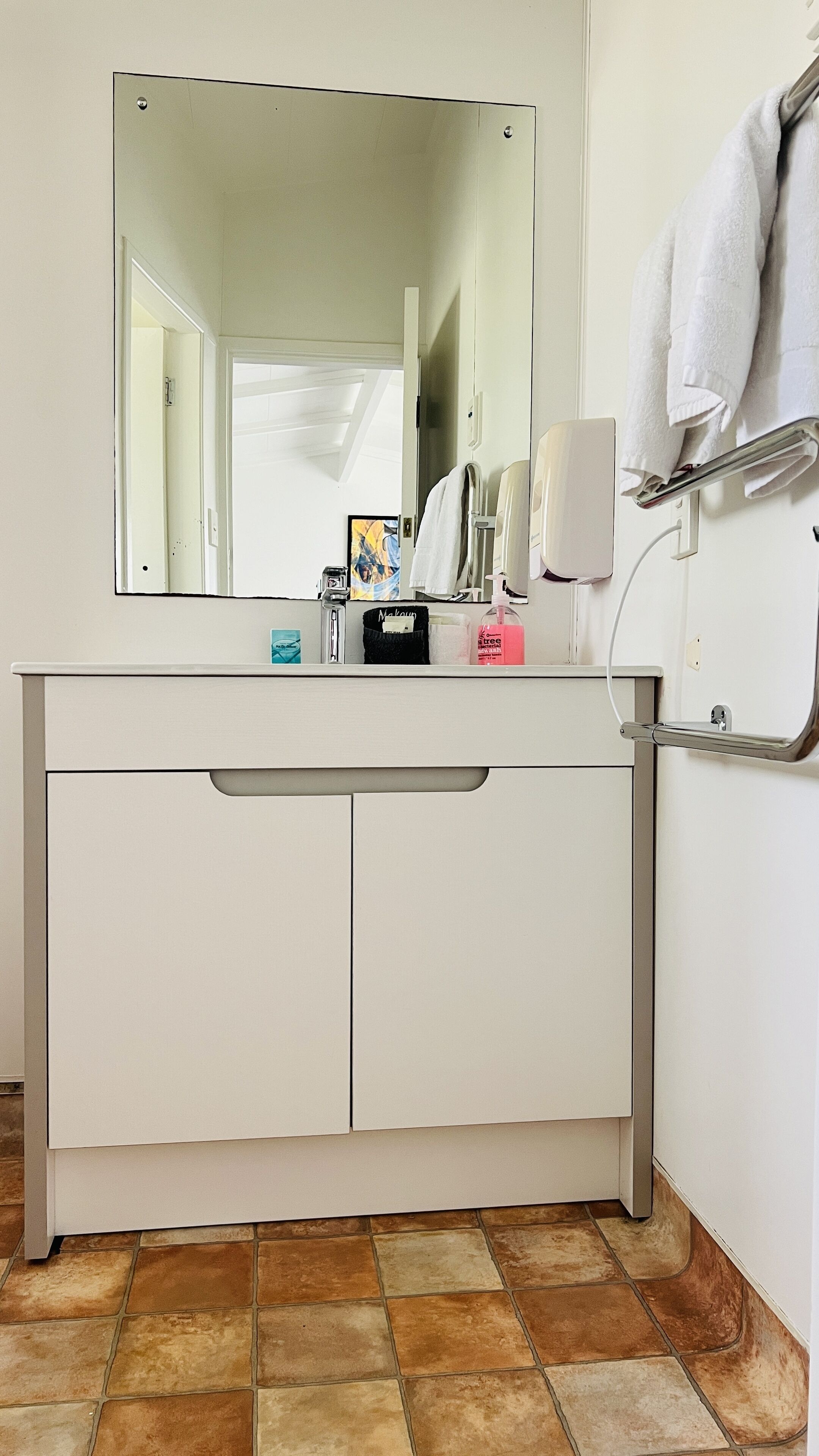 A bathroom with a white vanity, a large mirror, and a towel rack.
