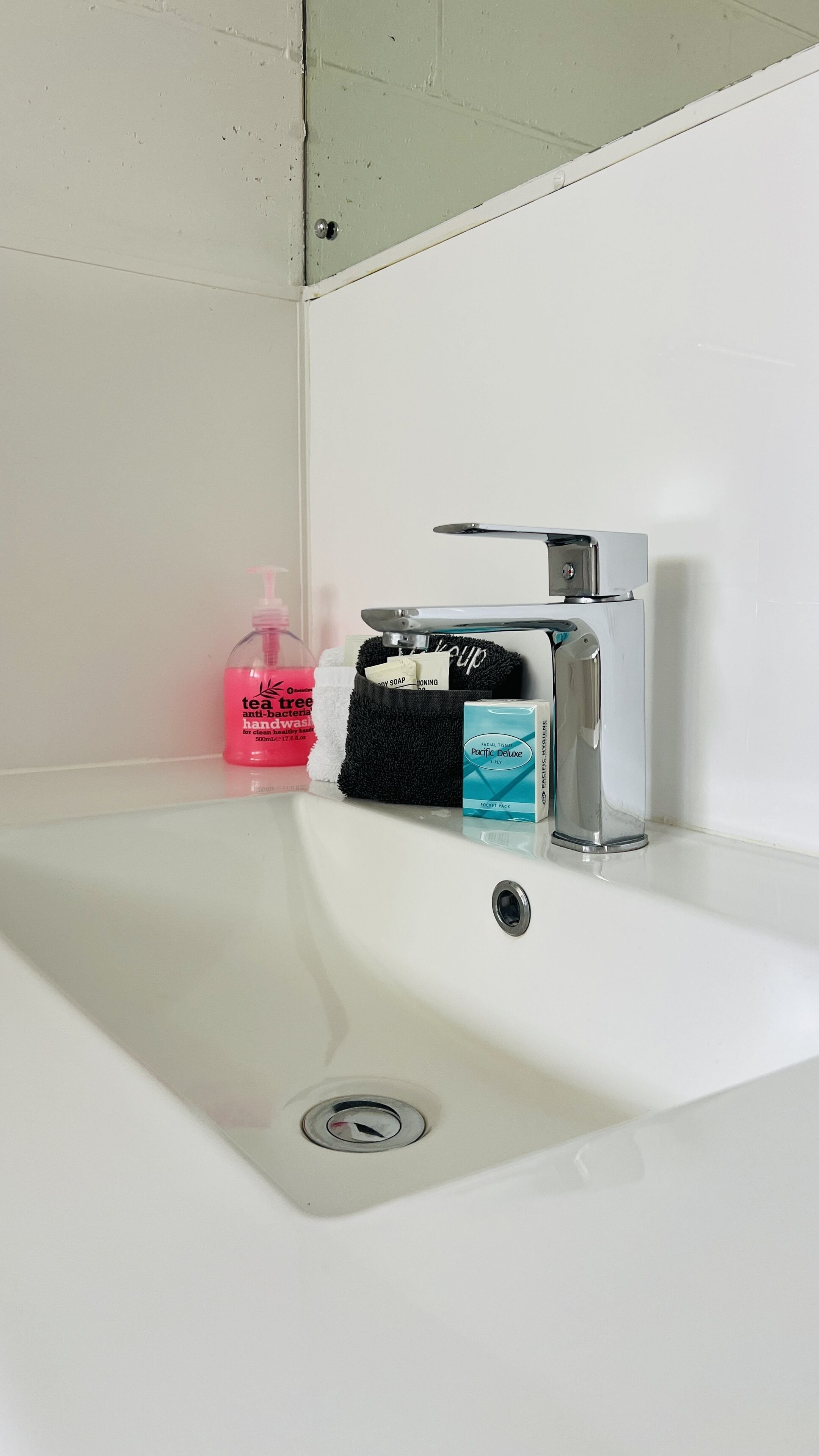 A bathroom sink with a mirror above it, a black towel, a soap dispenser, a facial tissue box, and a bottle of hand soap.