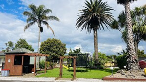 Un barrio residencial con una pequeña estructura de madera, un parque infantil y varias palmeras.